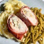 Sliced chicken breast filled with herby cream cheese and wrapped in prosciutto on a bed of mashed potatoes and green beans.