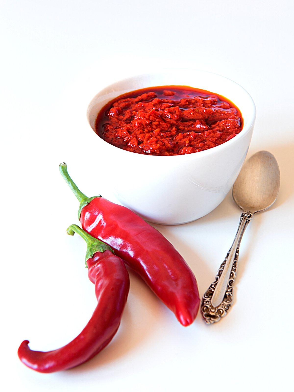A bowl of Harissa paste with fresh red chiles and spoon on the side.