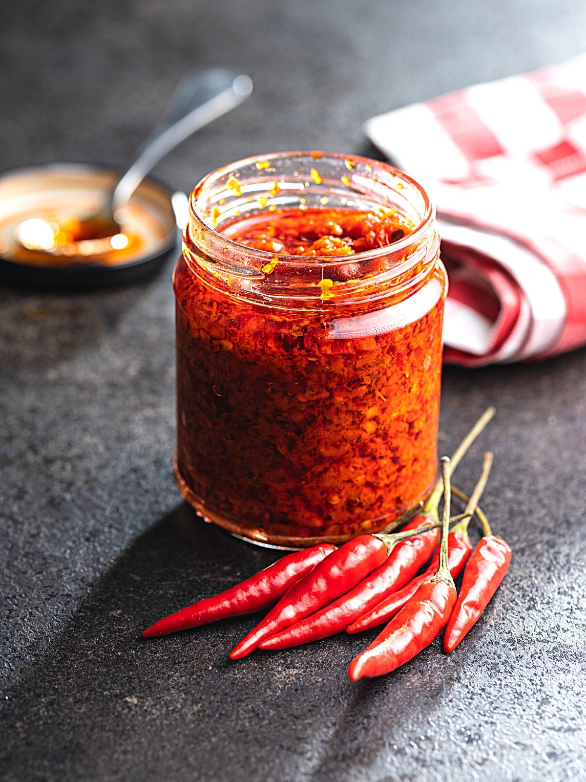 A jar of homemade chili paste with fresh red chilis on the side.