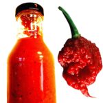 A bottle of Carolina Reaper hot sauce, along with a fresh Carolina pepper on the side.