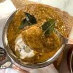 Egg curry in a copper bowl with a spoon of it lifting from it.