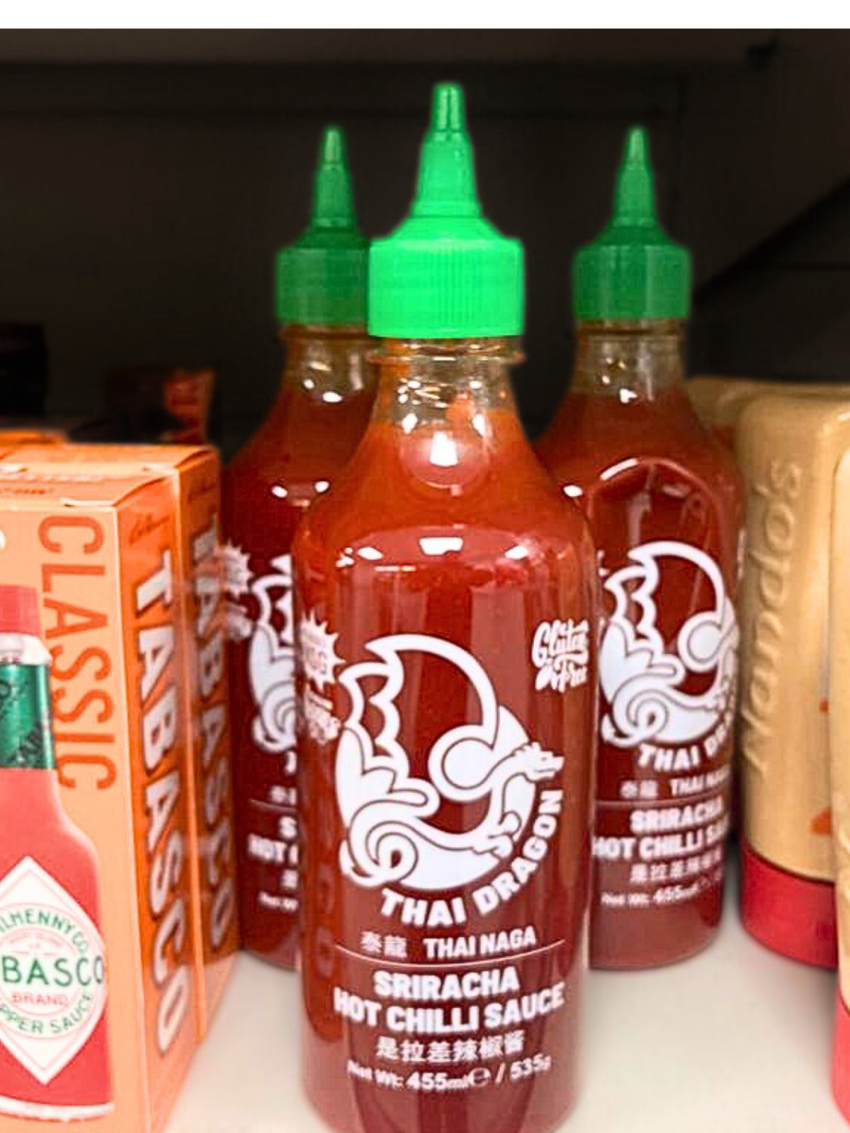 Sriracha sauce bottles on the shelves next to tabasco sauce bottles.