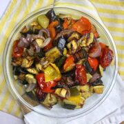 Mediterranean Roasted Vegetables in a glass plate on top of a white and yellow tea towel.