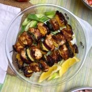 Chicken kabobs with vegetables in a glass plate with lemon wedges and chopped green onions.