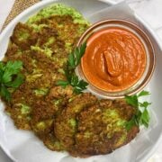 White plate with crispy broccoli fritters with Parmesan and a tomato basil dipping sauce in a glass bowl.