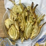 Slices of roasted fennel in a glass platter on top of a white cotton handkerchief.